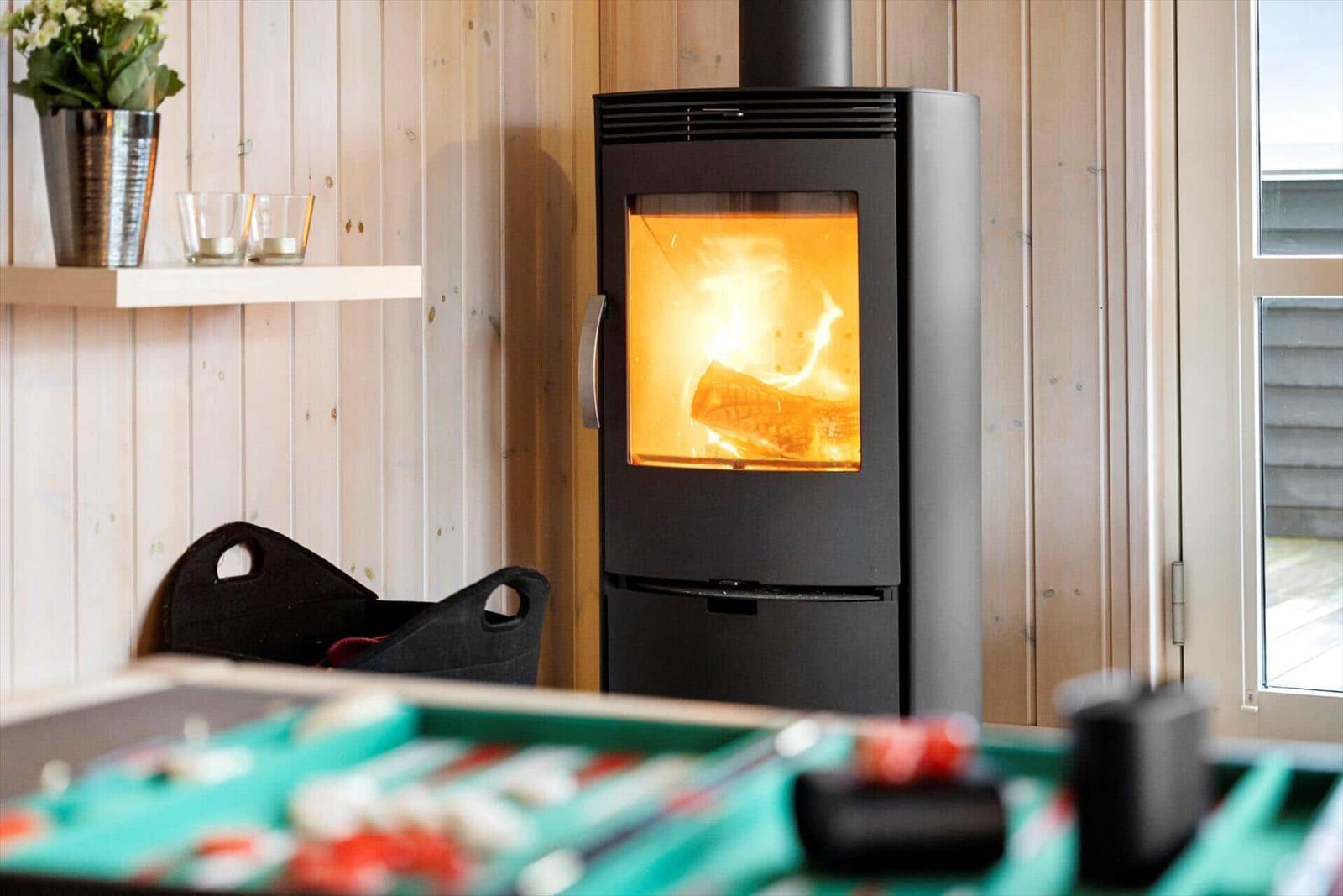 Kaminofen mit brennendem Holz, Holzwand und Tisch im Vordergrund.