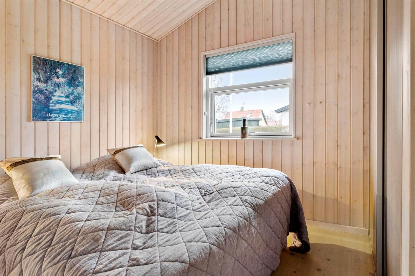 Schlafzimmer mit Holzwandverkleidung, Bett und Fenster mit Blick nach draußen.