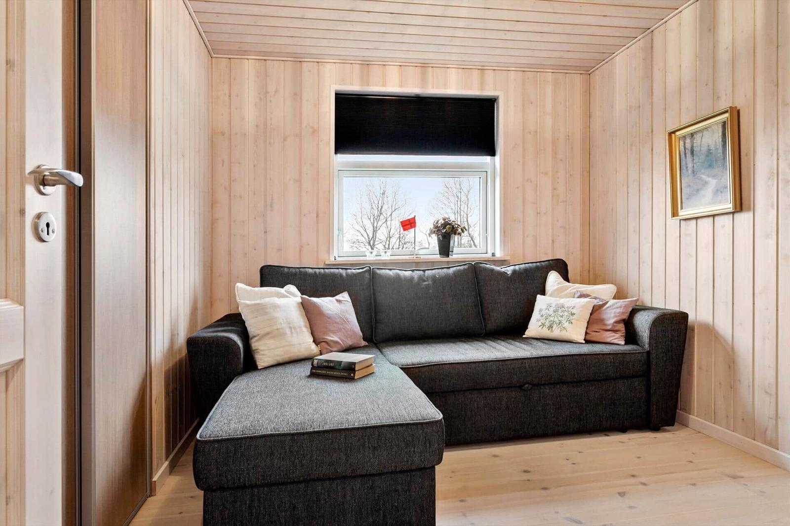 Ein Wohnzimmer mit einem grauen Sofa, Holzwänden und einem Fenster mit Blick auf Bäume.