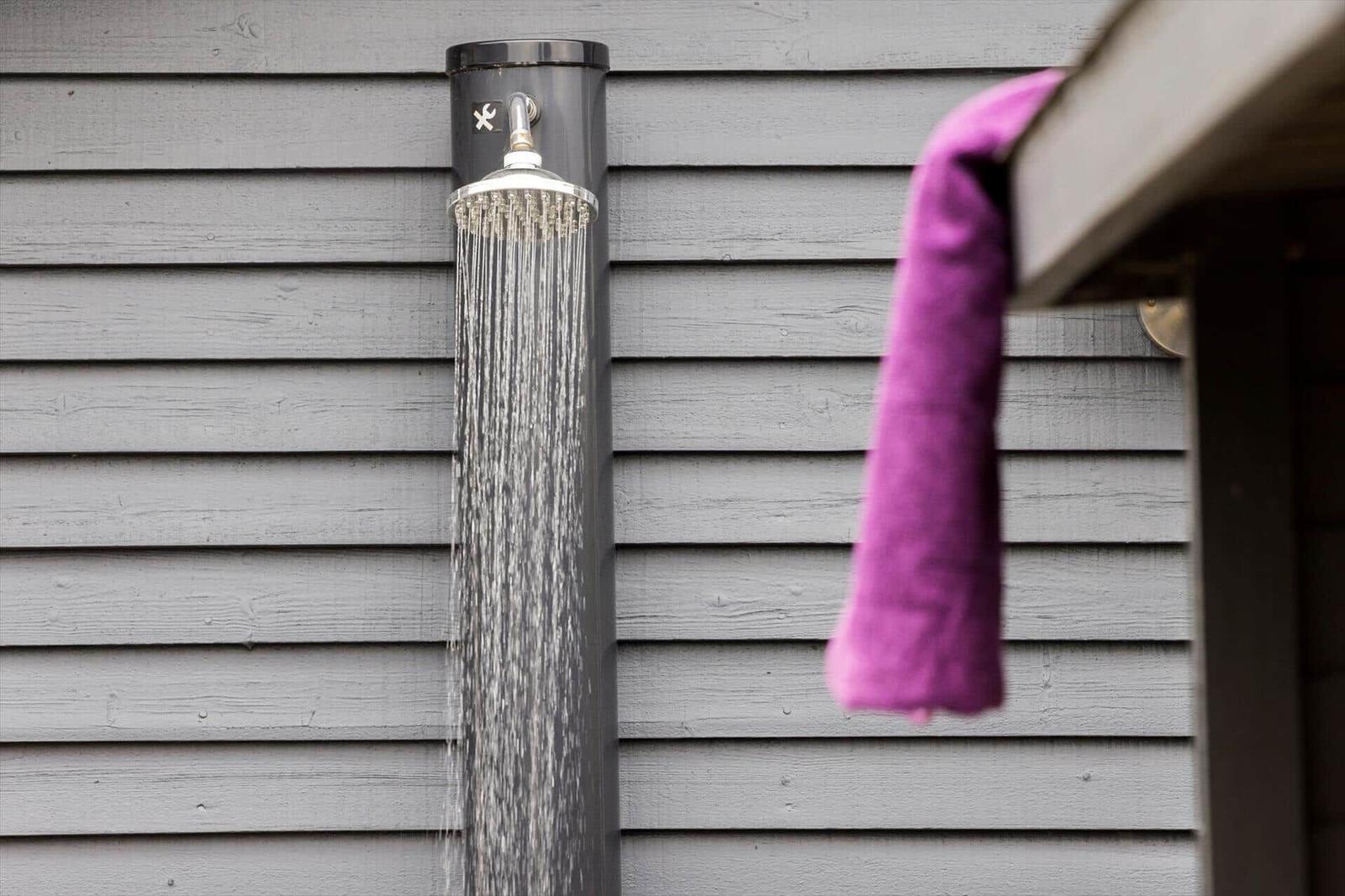 Außen-Dusche mit laufendem Wasser an grauer Wand, lila Handtuch hängt daneben.