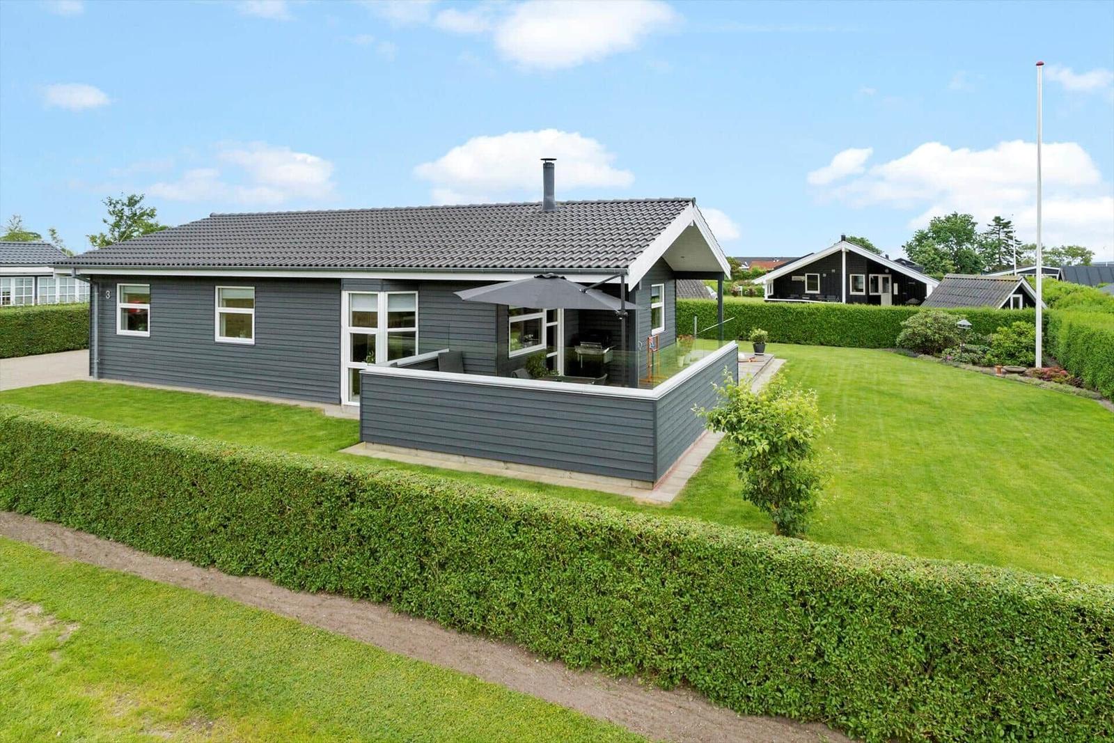 Ein graues Ferienhaus mit Terrasse und Garten. Hinterhof mit Hecke und Grillplatz.