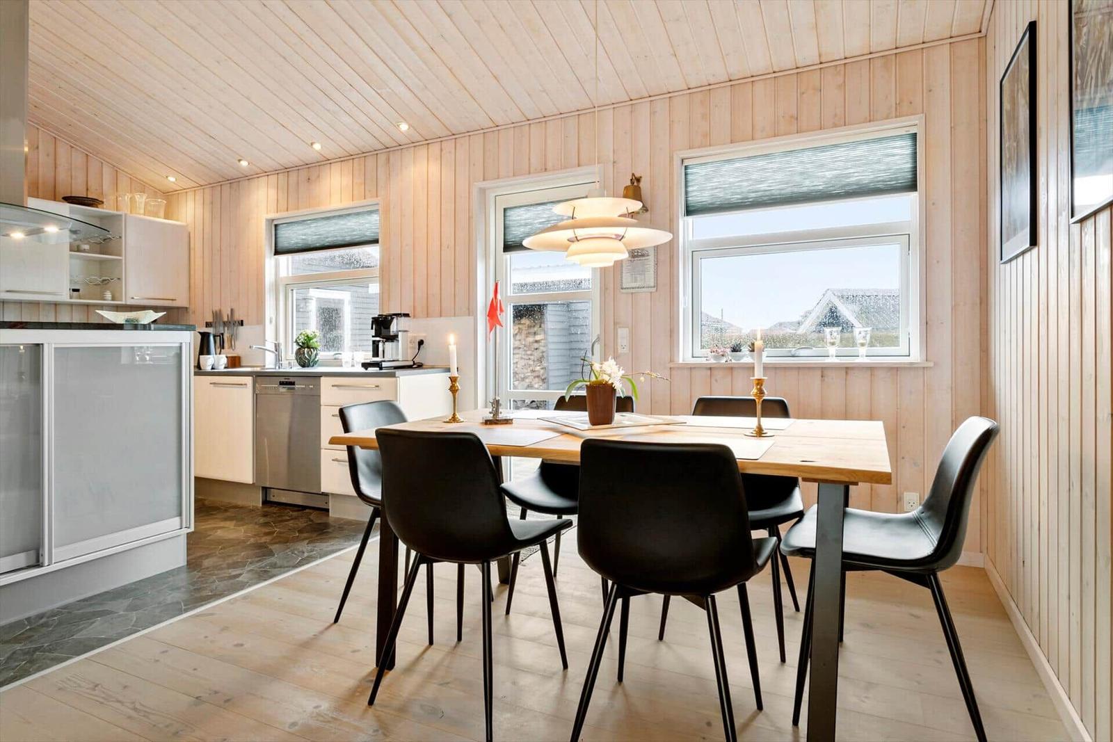 Essbereich mit Holztisch, schwarzen Stühlen und Küchenbereich mit Holzwänden.