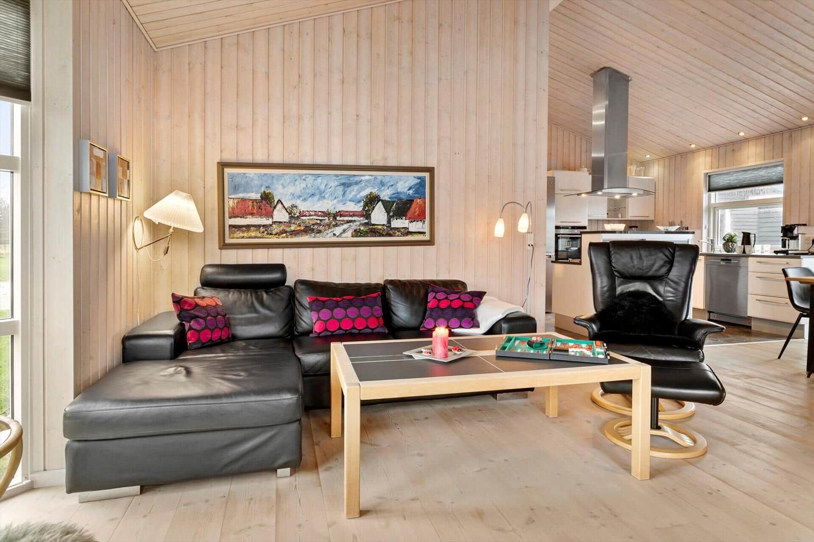 Wohnzimmer mit Ledersofa, Holztisch und Küchenbereich im Hintergrund.