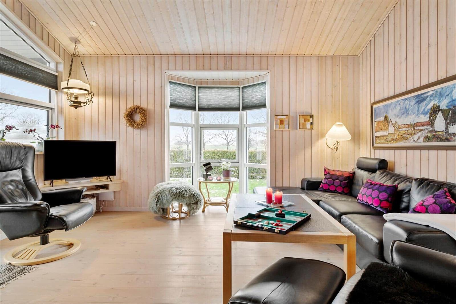 Wohnzimmer mit Holzwand, Sofa, Fernseher und Fensterblick.