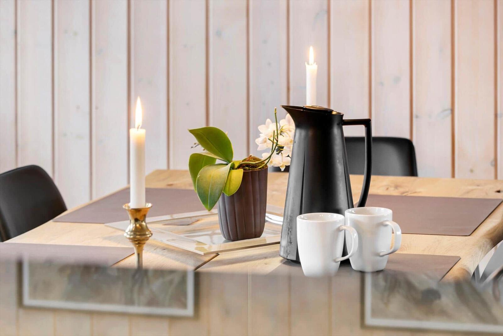Tisch mit zwei Kerzen, Kaffeekanne und Tassen auf Holzoberfläche.