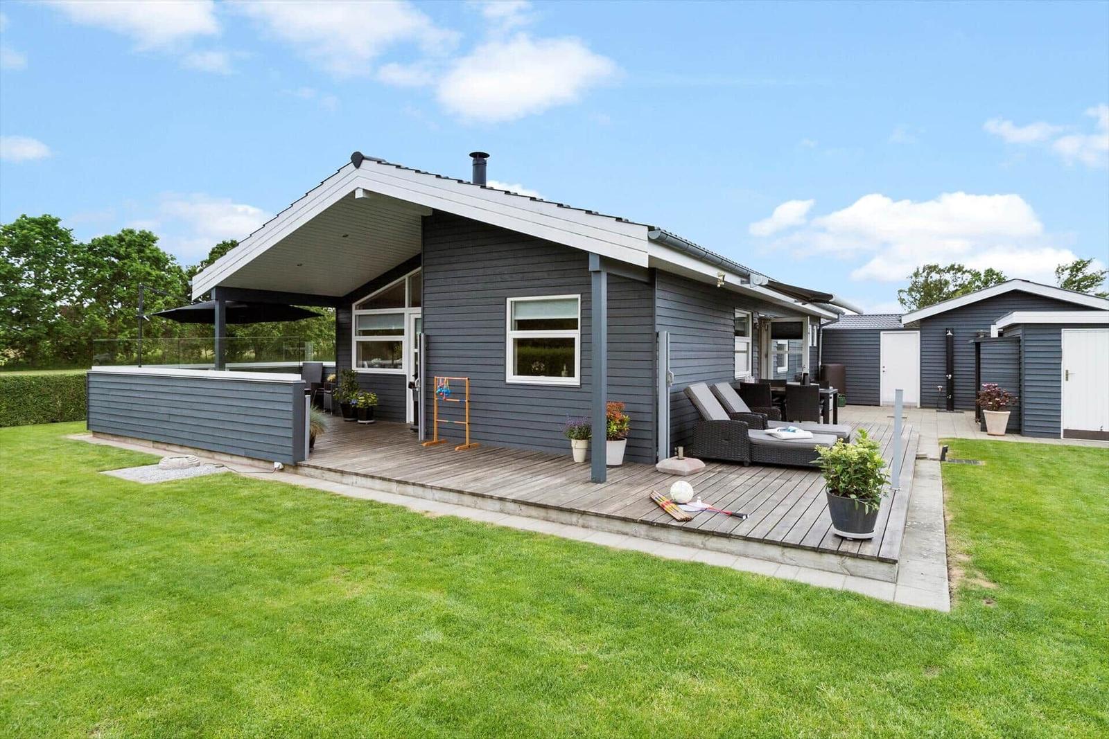 Moderne Ferienhaus mit Holzterrasse, Garten und Außensitzgelegenheiten.