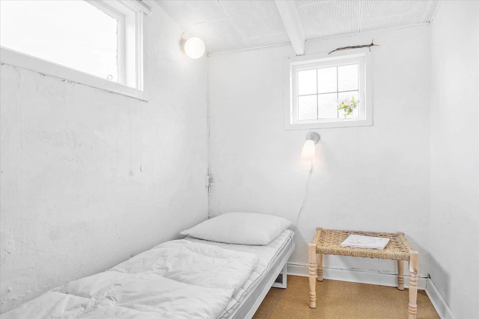 Ein Schlafzimmer mit Bett, zwei Fenstern und einem Hocker.
