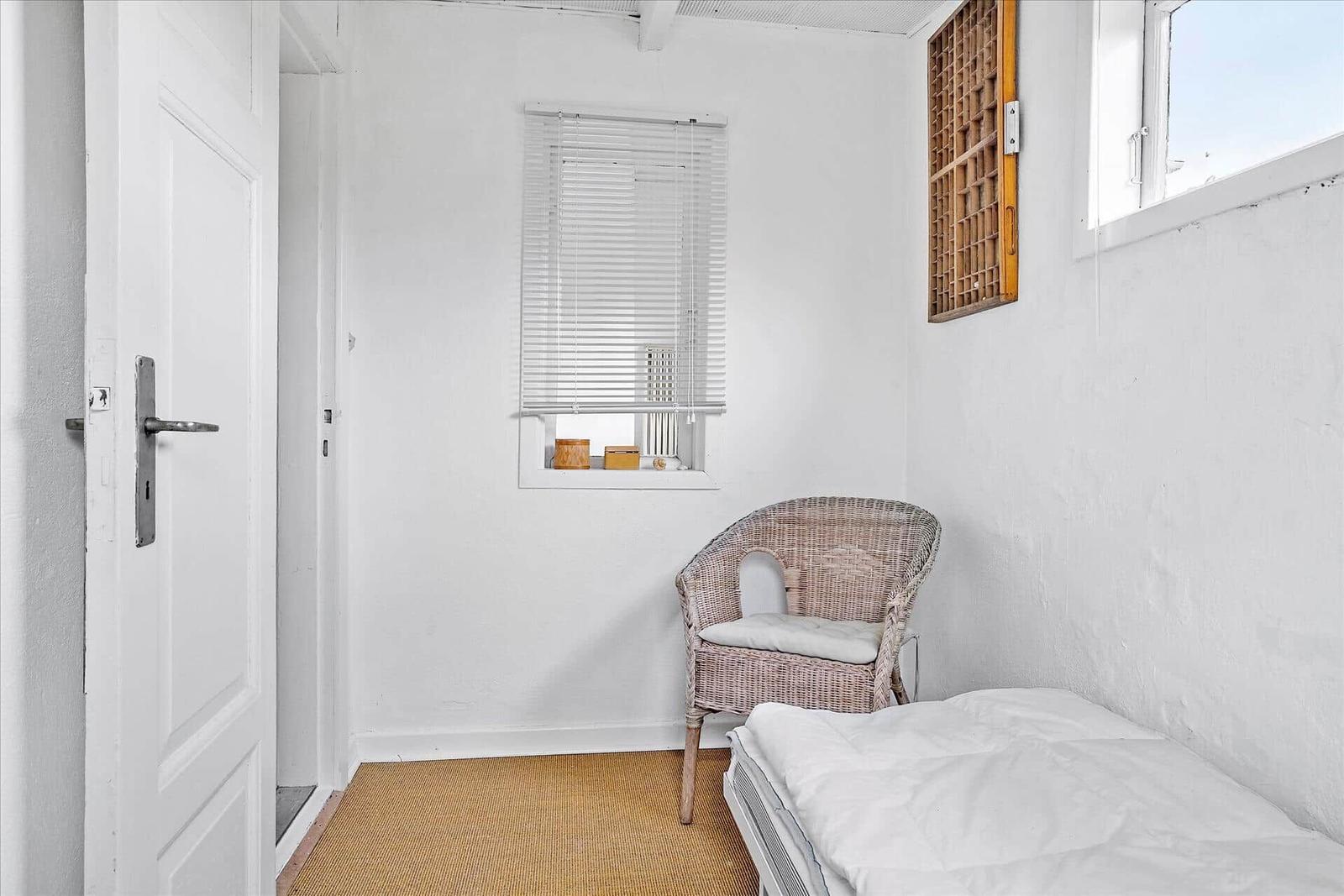 Ein Schlafzimmer mit Bett, Stuhl und Fenster. Wand und Boden sind weiß.