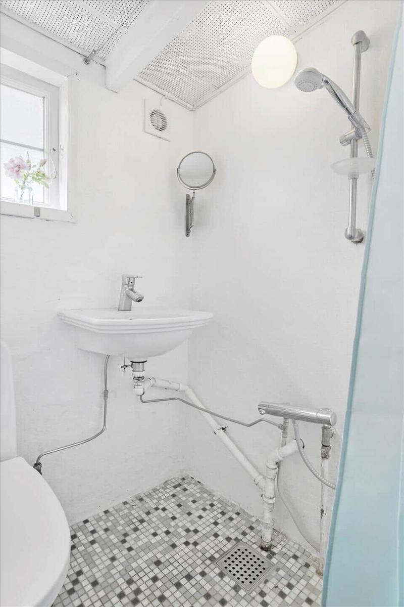 Badezimmer mit Waschbecken, Dusche und Toilette. Bodenfliesen und Fenster sichtbar.