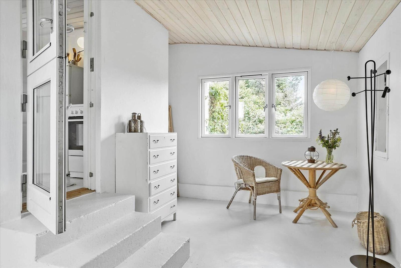 Raum mit weißen Wänden, Holzdecke, Fenster und Möbel. Treppen führen zur Küche.