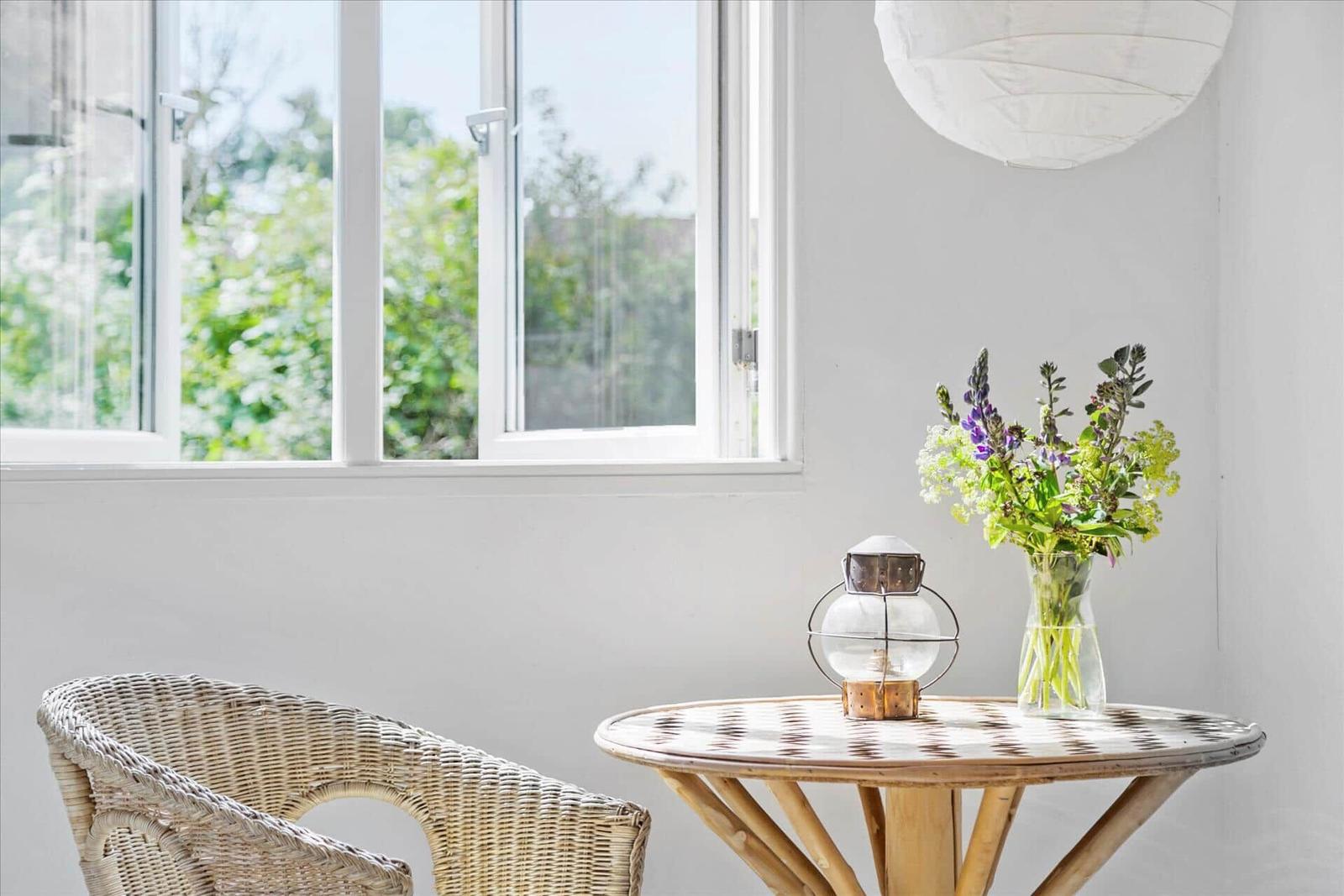 Ein runder Tisch mit Stuhl vor einem Fenster. Darauf steht eine Laterne und eine Vase mit Blumen.