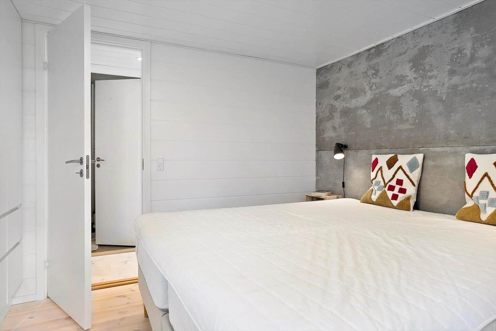 Schlafzimmer mit Bett, Kopfkissen und Bettkopfteil an Betonwand.