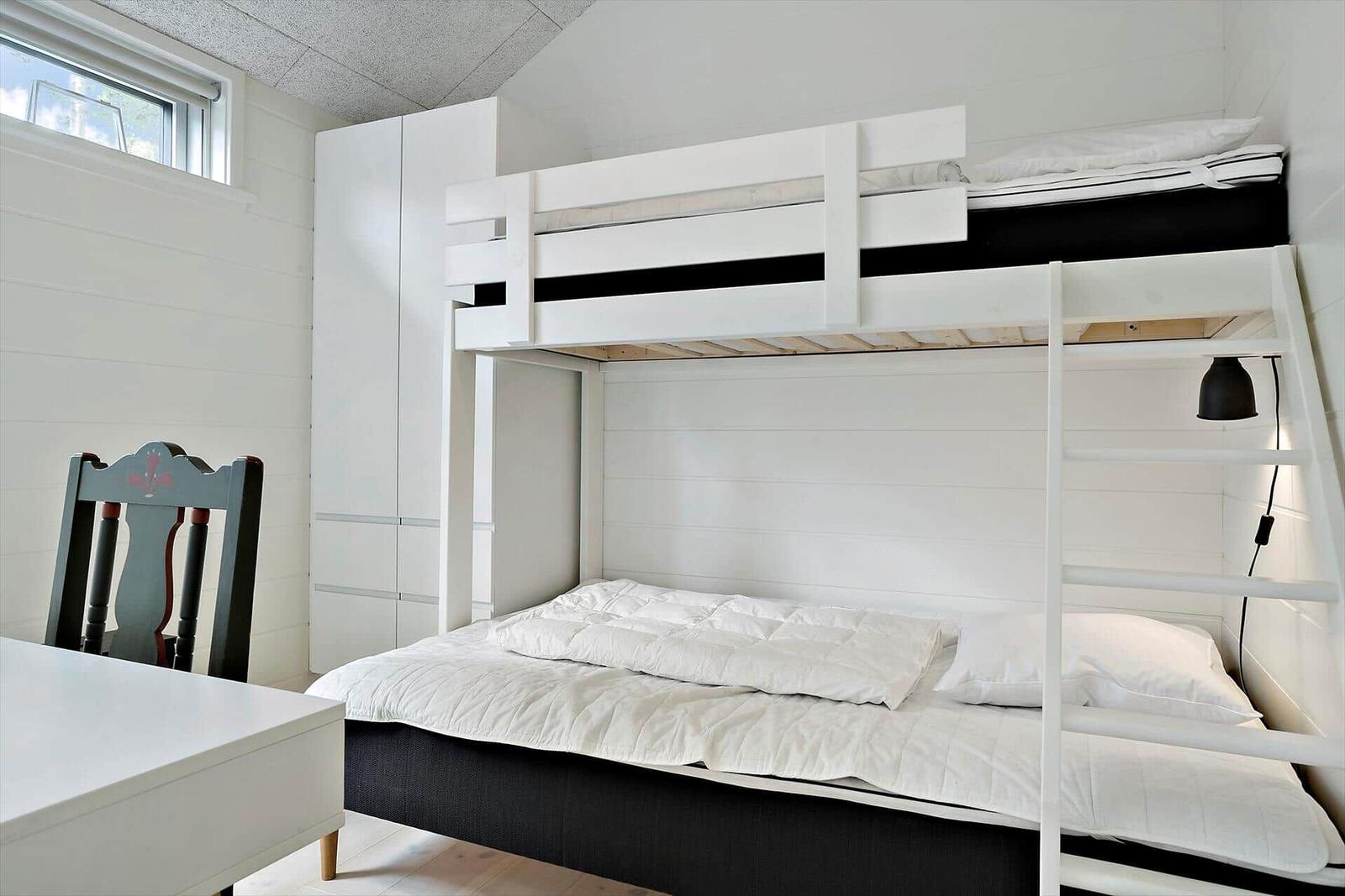 Zimmer mit Doppelstockbett, Schreibtisch und Stuhl. Weiße Wände und Holzboden.