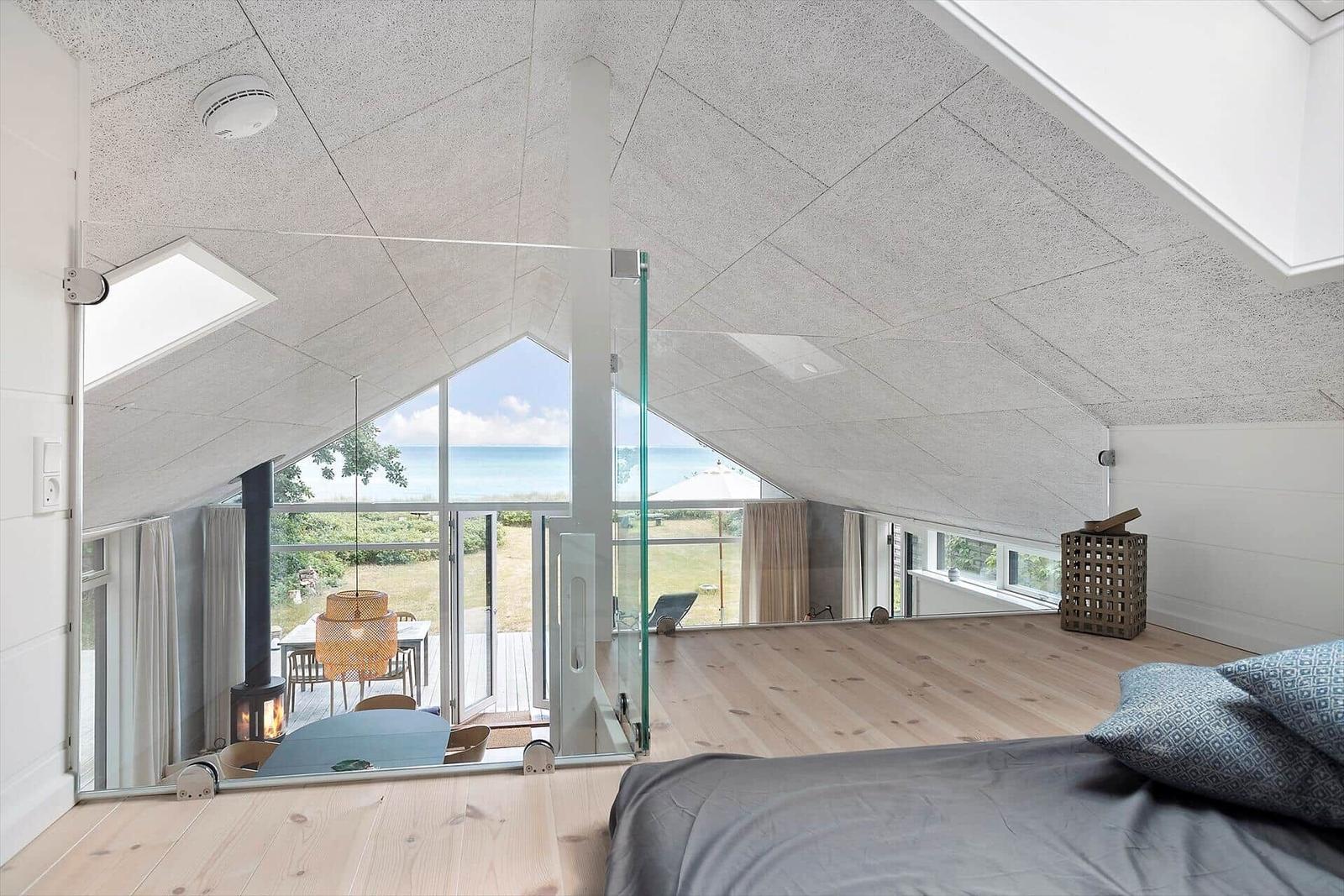 Schlafzimmer mit Blick auf den Strand und Terrasse. Holzboden, Glasgeländer und Dachschräge.