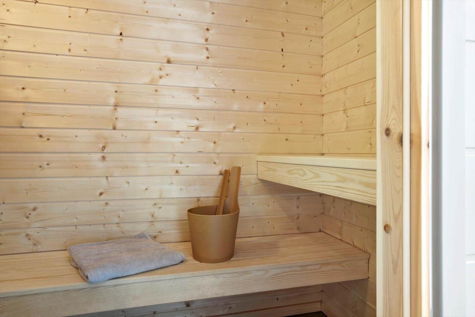 Sauna mit Holzbank, Handtuch und Eimer mit Besen.