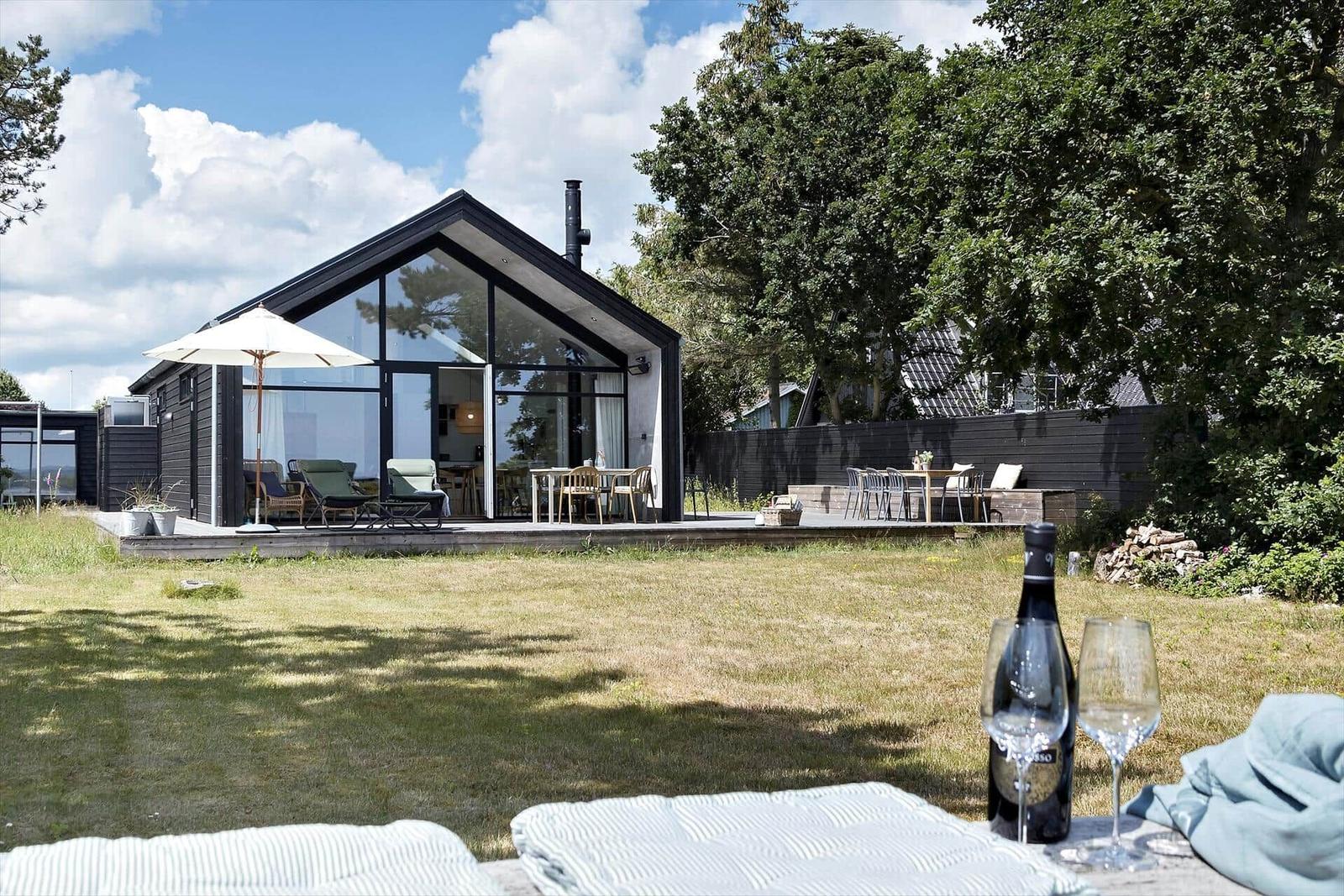 Moderne Villa mit großem Garten und Terrasse. Im Vordergrund stehen ein Weinglas und eine Flasche.