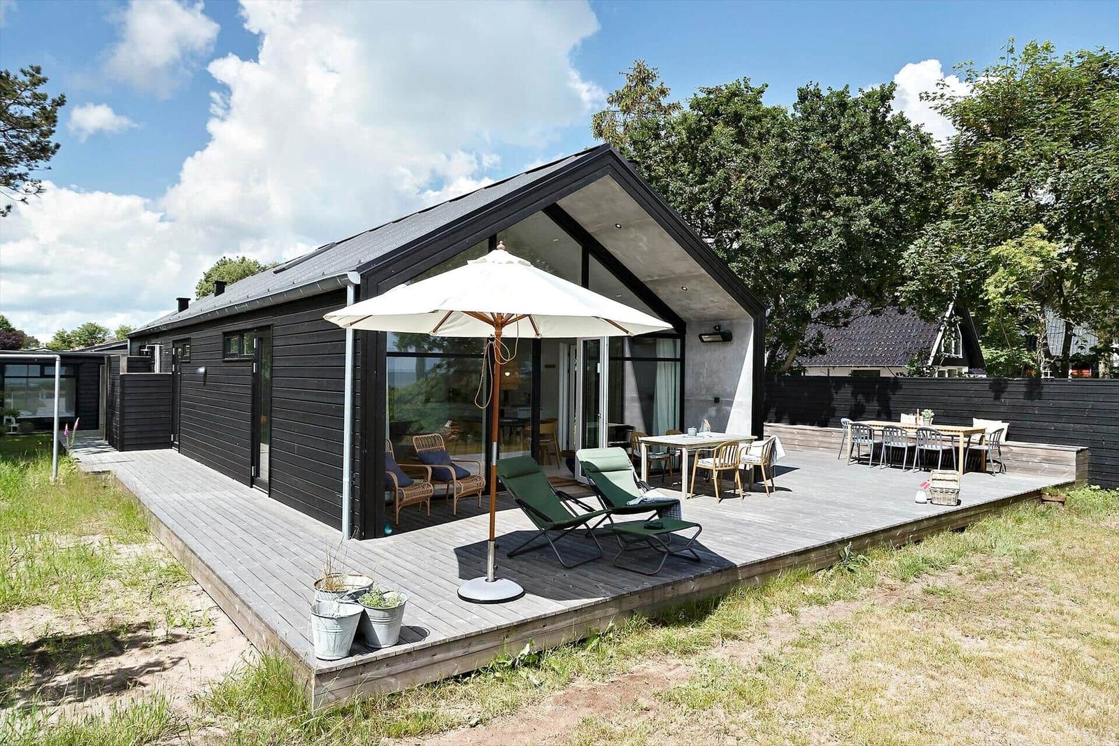 Moderne Villa mit großem Holzdeck, Liegestühlen und Tisch unter freiem Himmel.