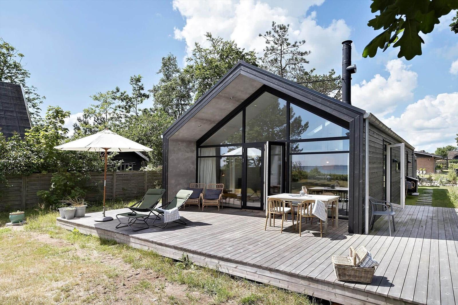 Moderne Hütte mit großem Holzterrasse, Sitzgelegenheiten und Blick auf die Landschaft.