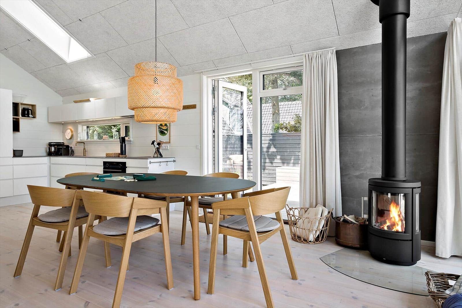Essbereich mit Holztisch, Stühlen und Kaminofen. Durchgang zur Küche und Terrasse.