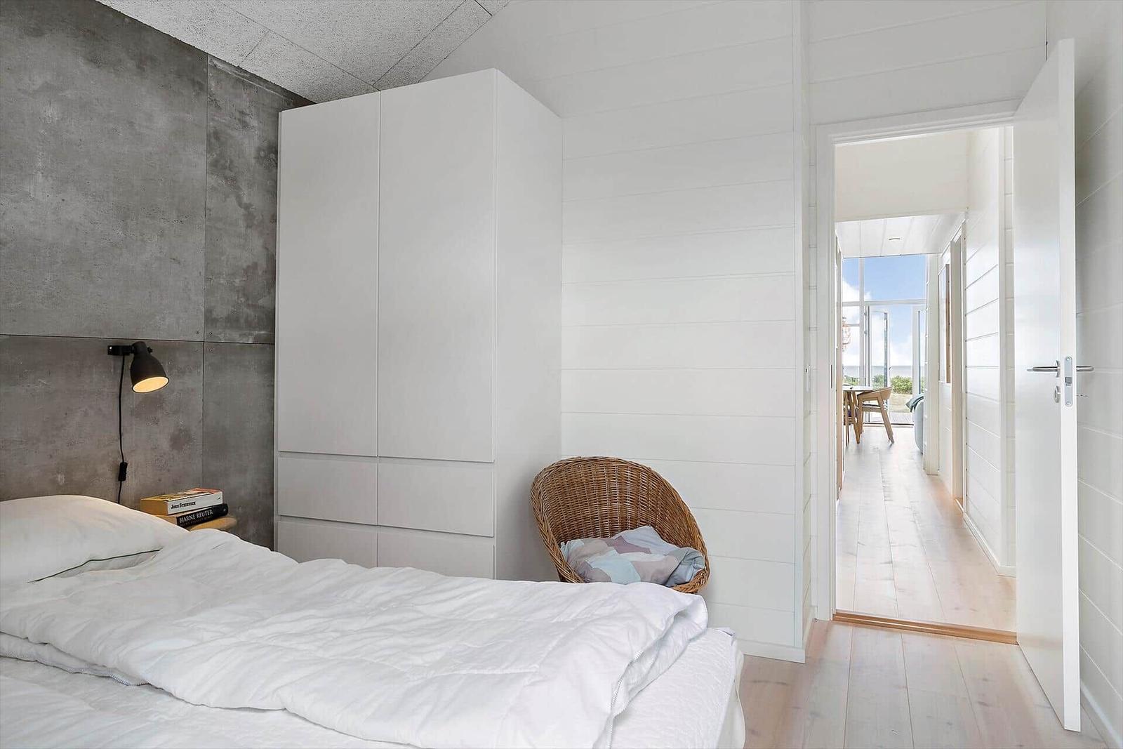 Schlafzimmer mit weißem Bett, Kleiderschrank und Stuhl. Durchgang zur Terrasse mit Blick aufs Meer.