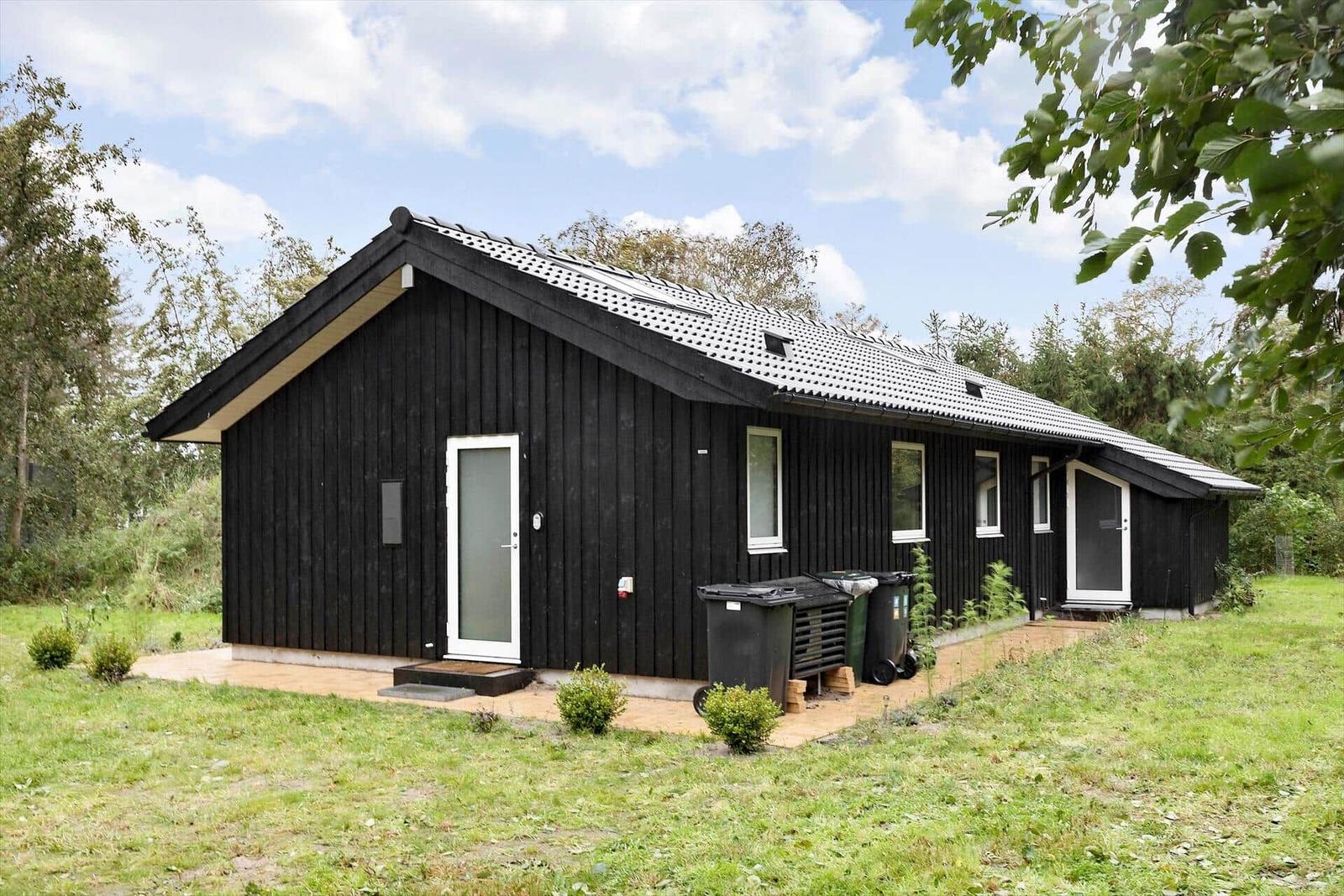 Black wooden house with white windows and door. Surrounded by green, sky with clouds.