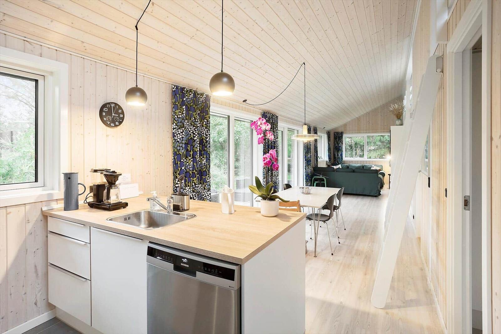 Kitchen with dining area and living room in the background. Wooden walls and floor.