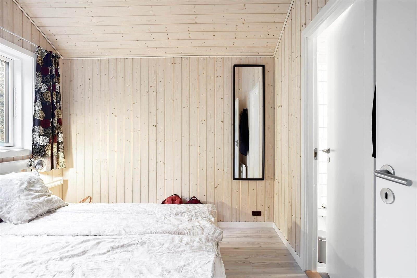 Bedroom with wooden walls, bed, mirror, and window with curtain.