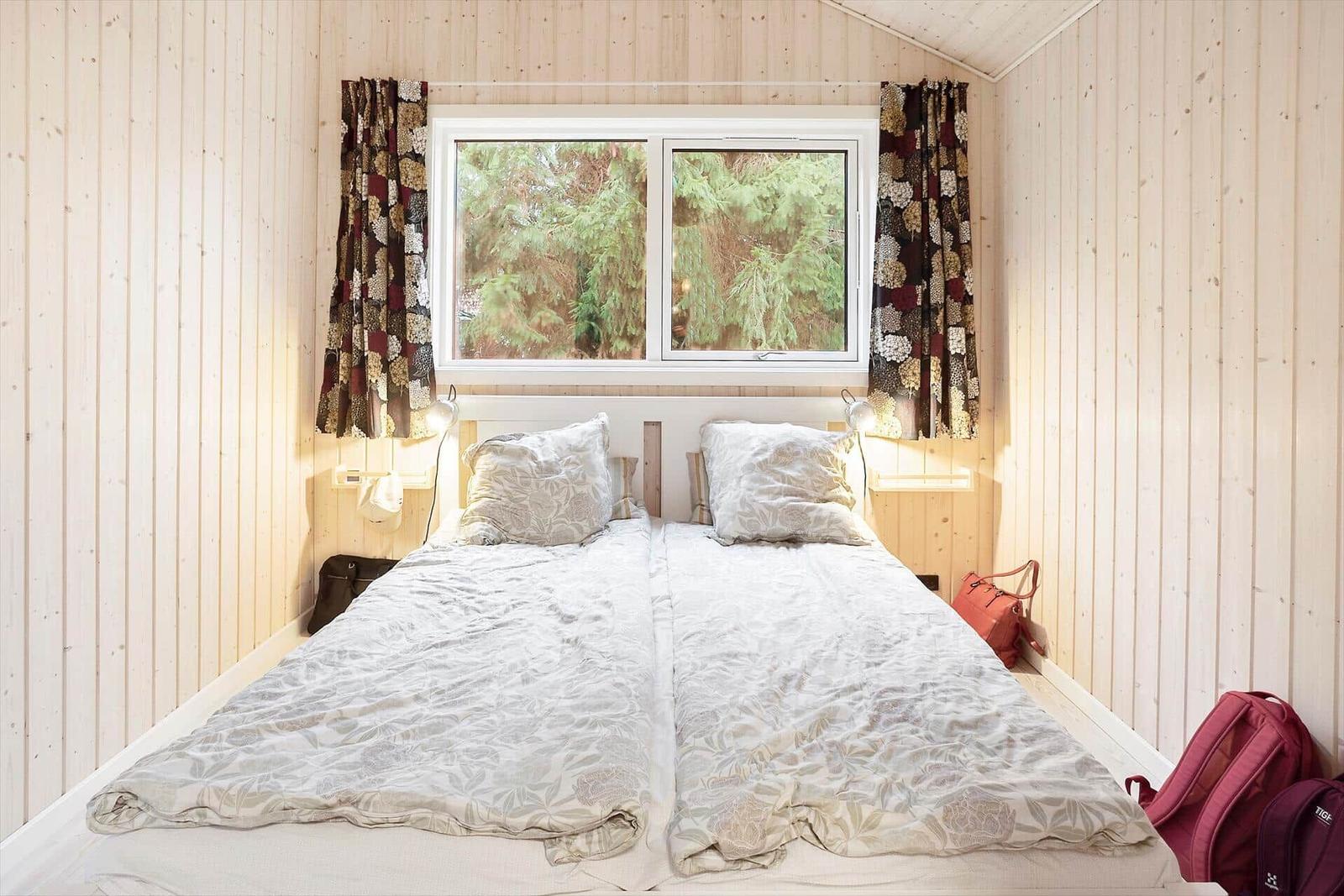 Bedroom with double bed, wooden walls, and window with view of trees.