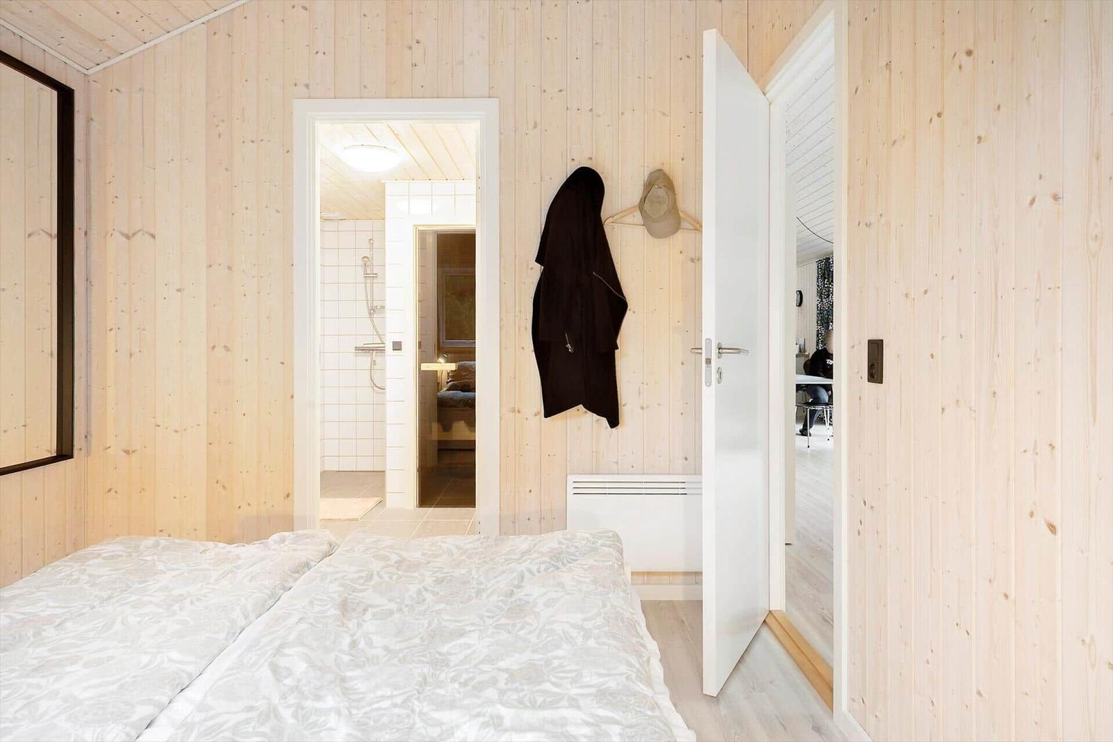 Bedroom with wooden walls, bed, and view into bathroom and living area.