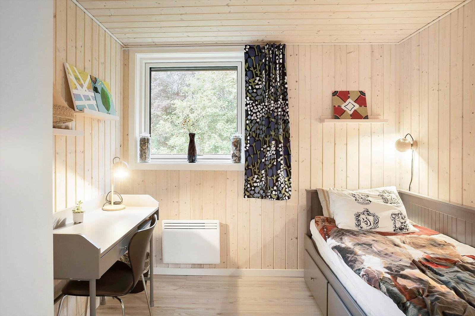 Bedroom with bed, desk, and window overlooking forest.