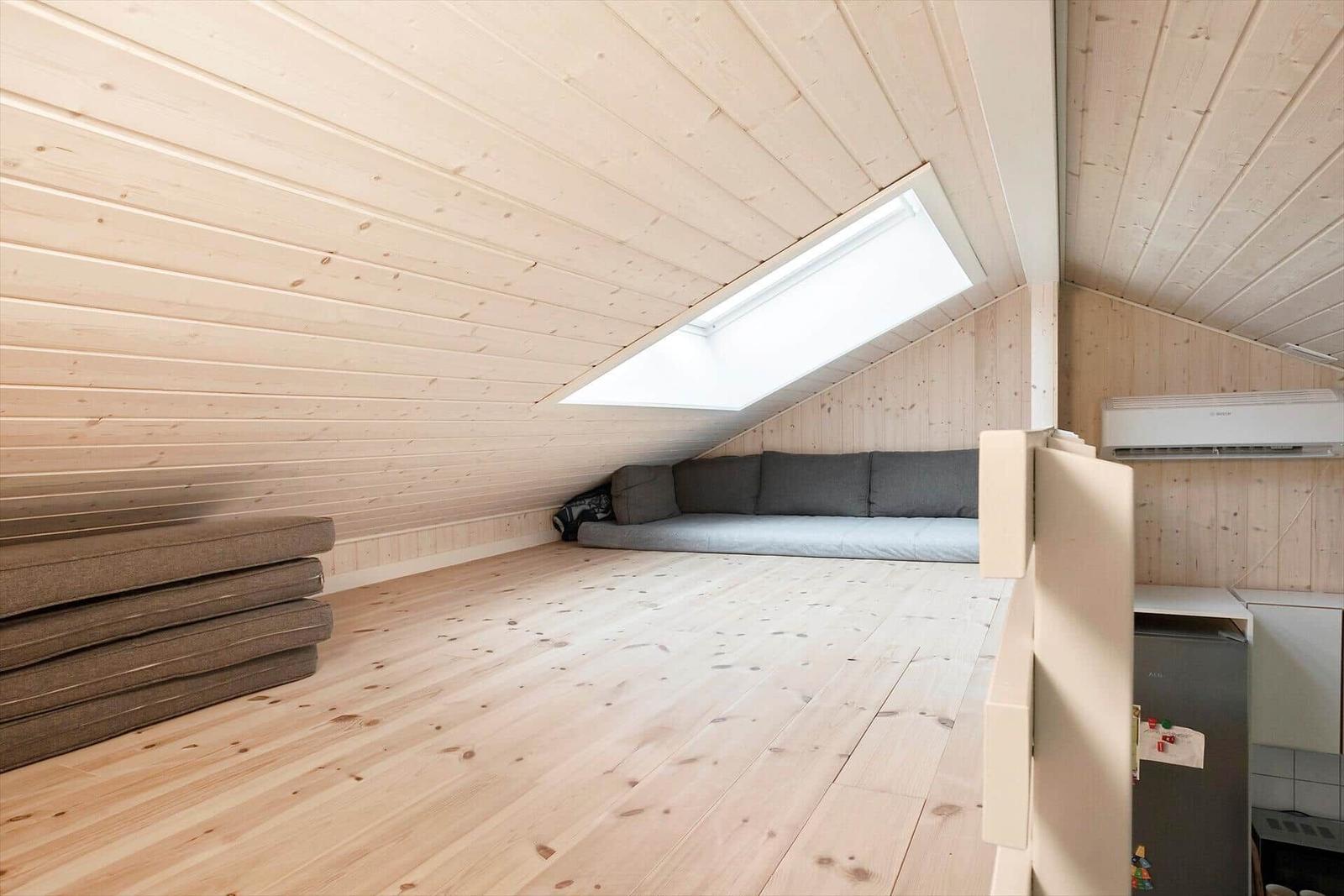 Attic with wooden ceiling, sofa bed, and skylight. Kitchen area with refrigerator.