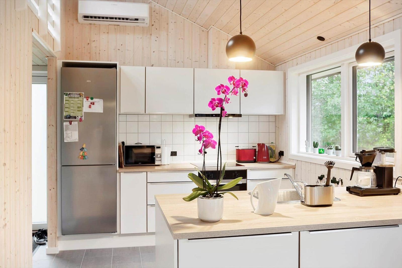 Kitchen with wooden walls, refrigerator, worktop, and window with view of greenery.