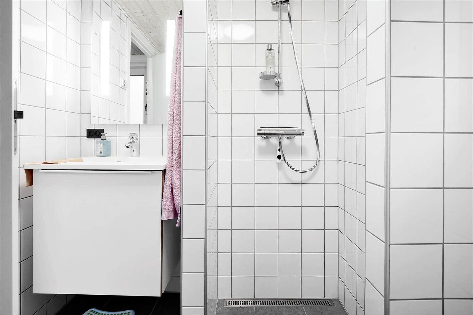 Bathroom with shower and sink. White tiles and mirror.