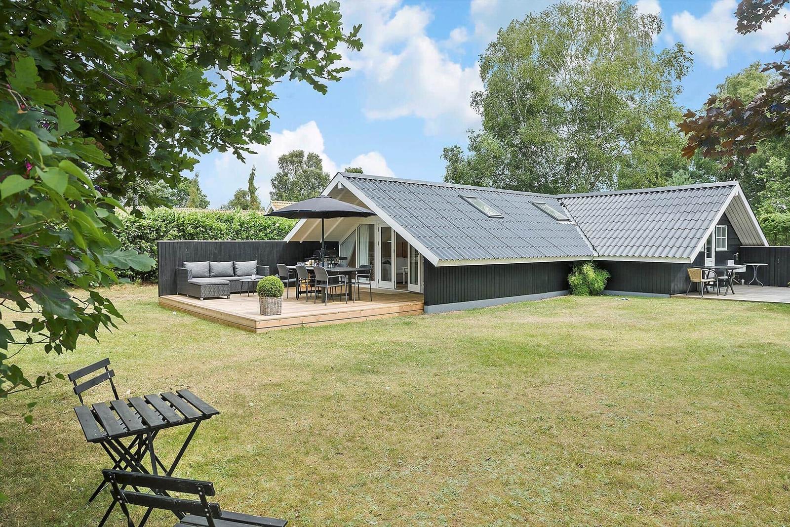 Modernes Haus mit Terrasse, Garten und Grillplatz unter blauem Himmel.