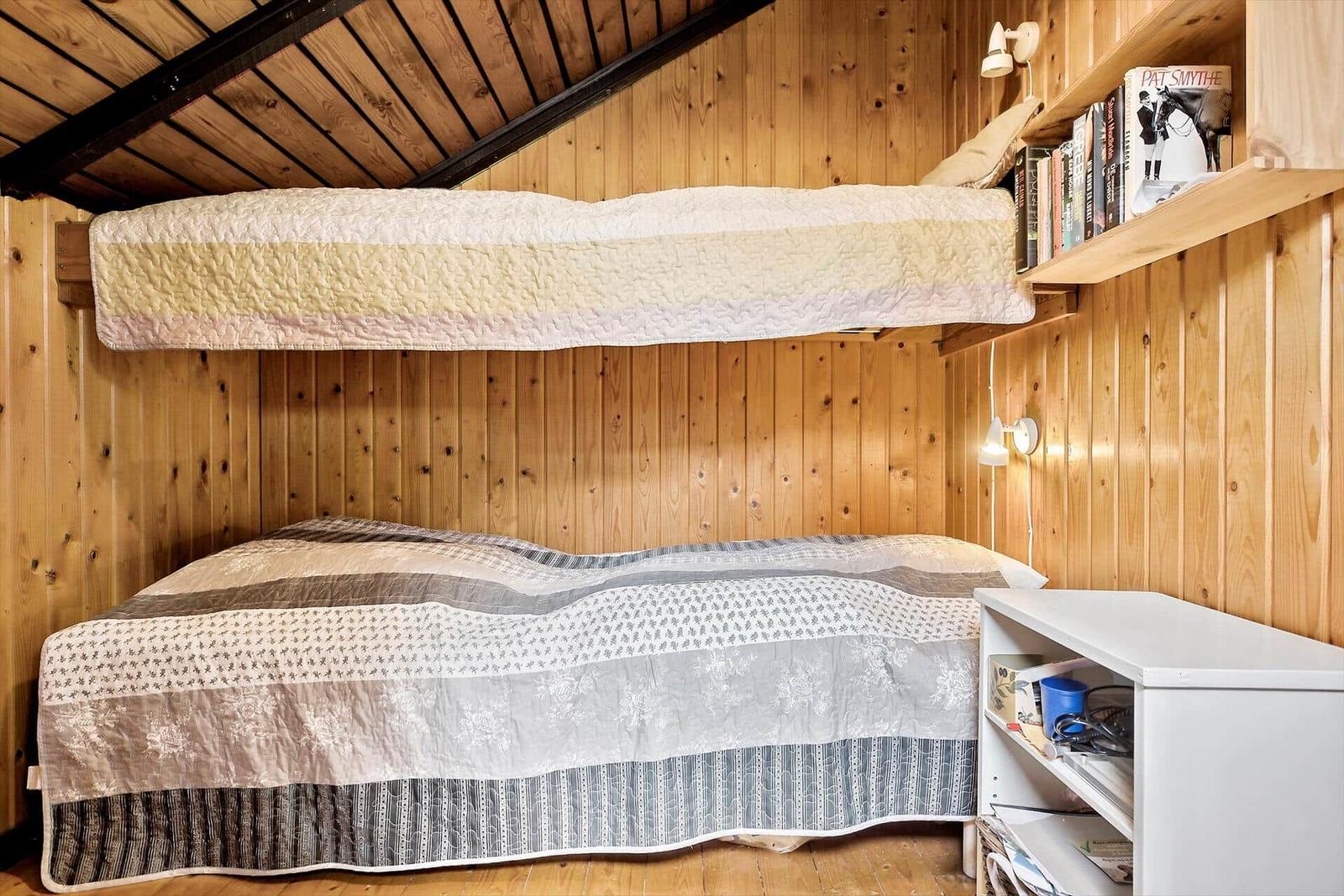 Zimmer mit Doppelbett und oberem Bett, Holzwände und Regal mit Büchern.