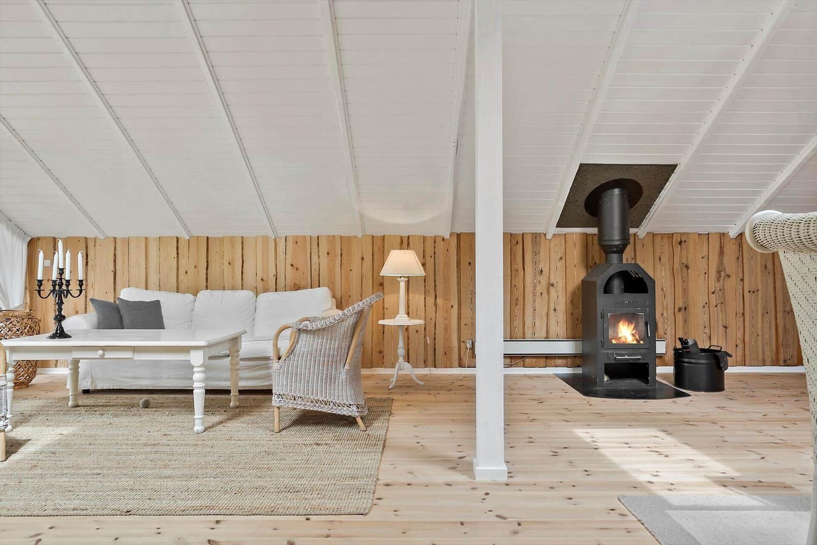 Wohnzimmer mit Sofa, Sessel und Kaminofen an Holzwand