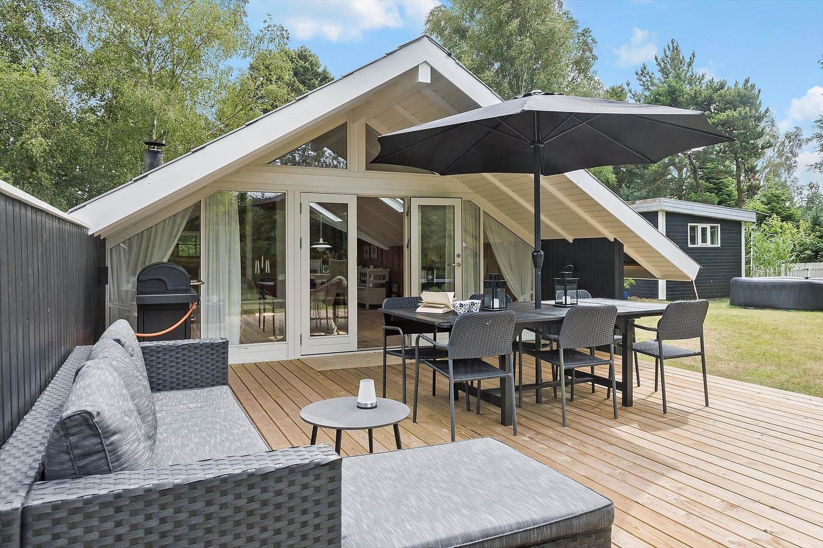 Terrasse mit Sitzgruppe, Tisch, Sonnenschirm und Grill. Durchgehende Glasfront zum Innenraum.
