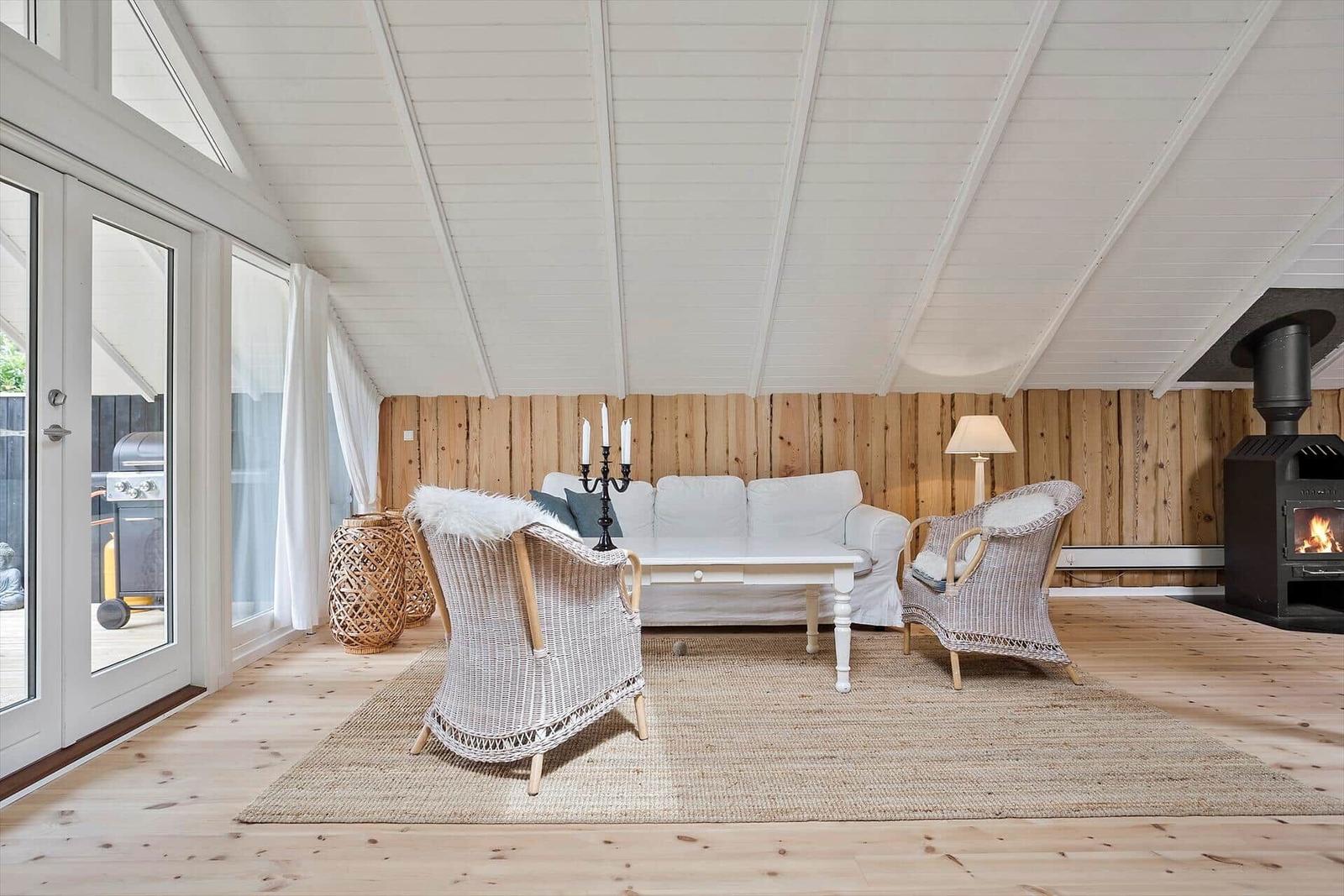 Wohnzimmer mit Sitzgruppe, Kamin und Holzwand. Durchgang zur Terrasse mit Grill.