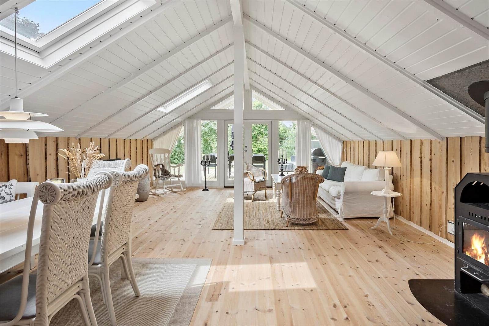 Wohnraum mit Holzfußboden, weißen Möbeln und Kamin. Dachfenster und Glastüren bieten viel Licht.