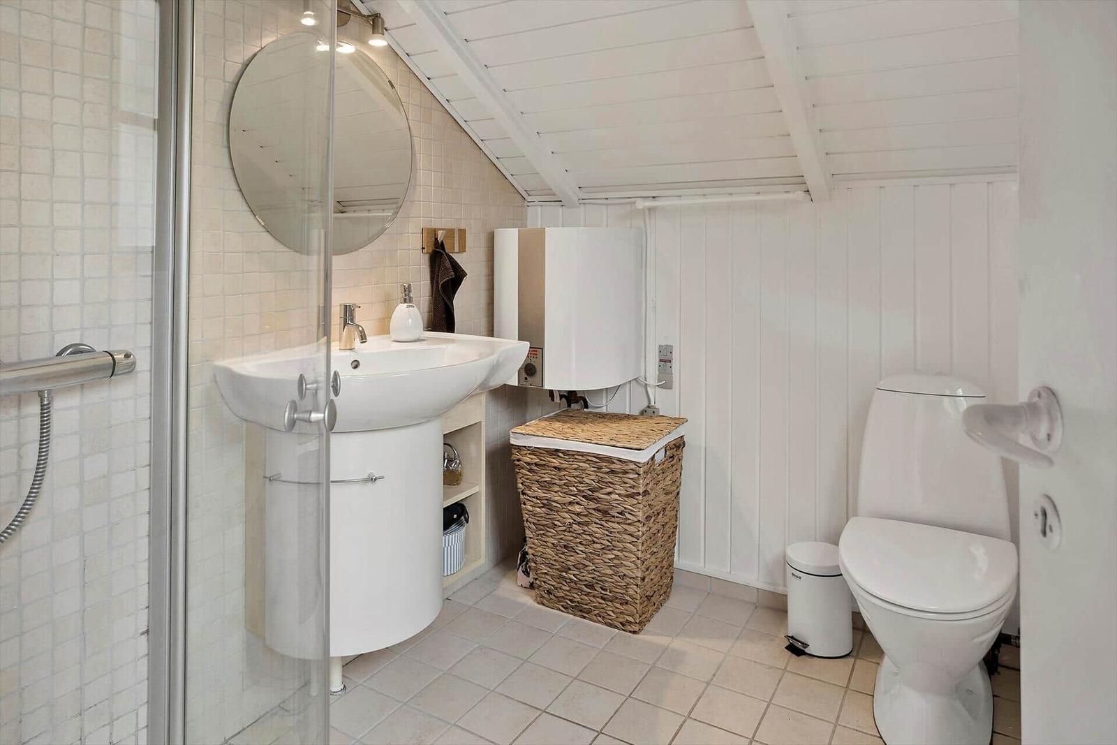 Badezimmer mit Dusche, Waschbecken und Toilette. Weiße Wände und Bodenfliesen.