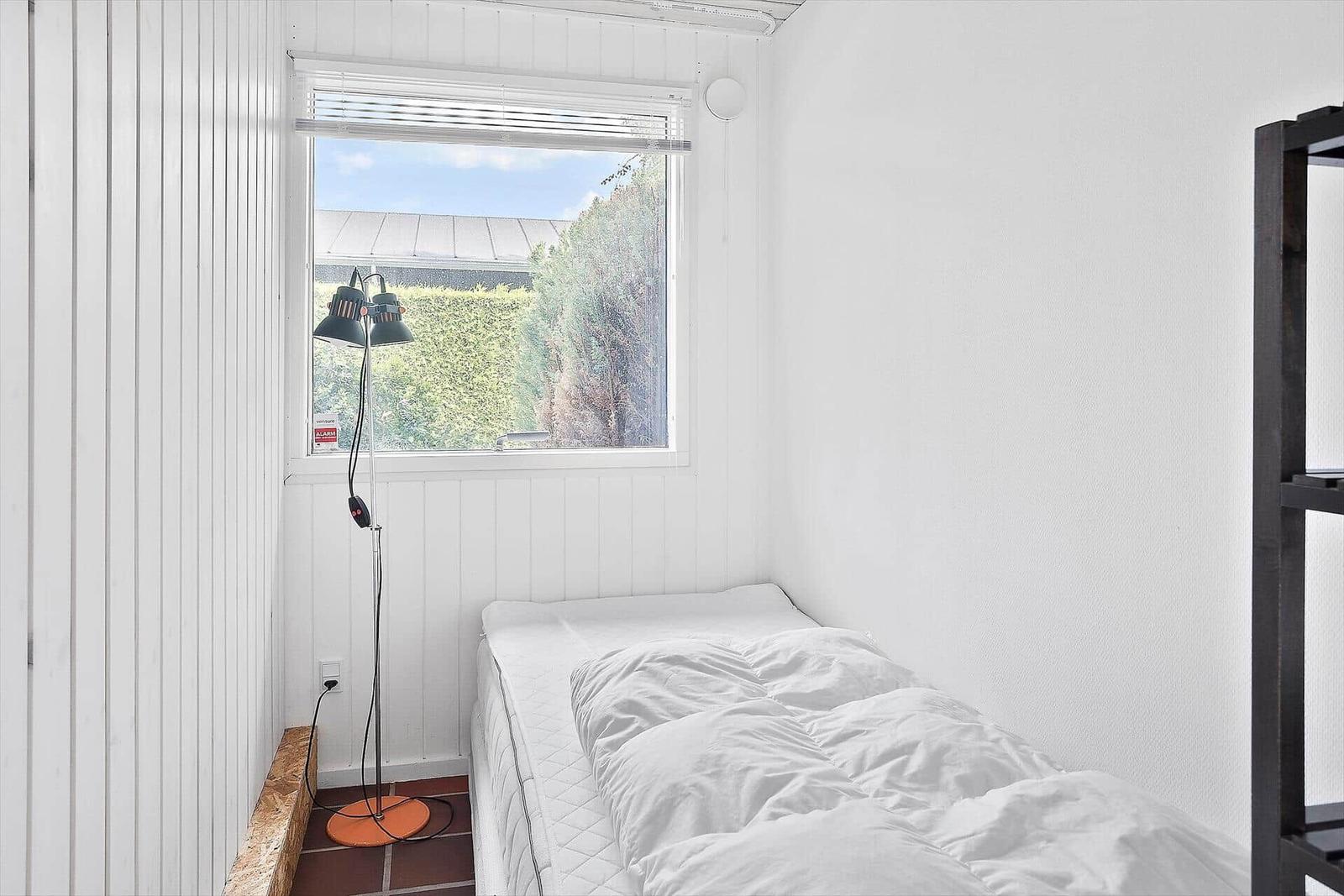 Ein Schlafzimmer mit weißer Wand, einem Bett und einem Fenster mit Blick auf Grün.