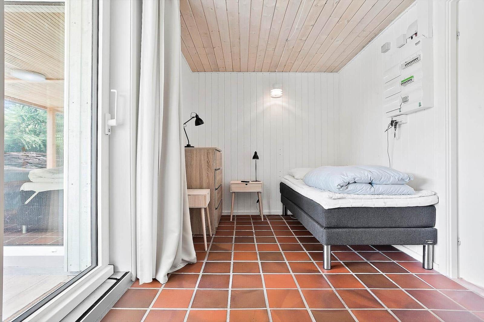 Schlafzimmer mit Bett, Nachttisch und Schrank. Terrasse über Schiebetür. Holzdecke und Terrakottaboden.