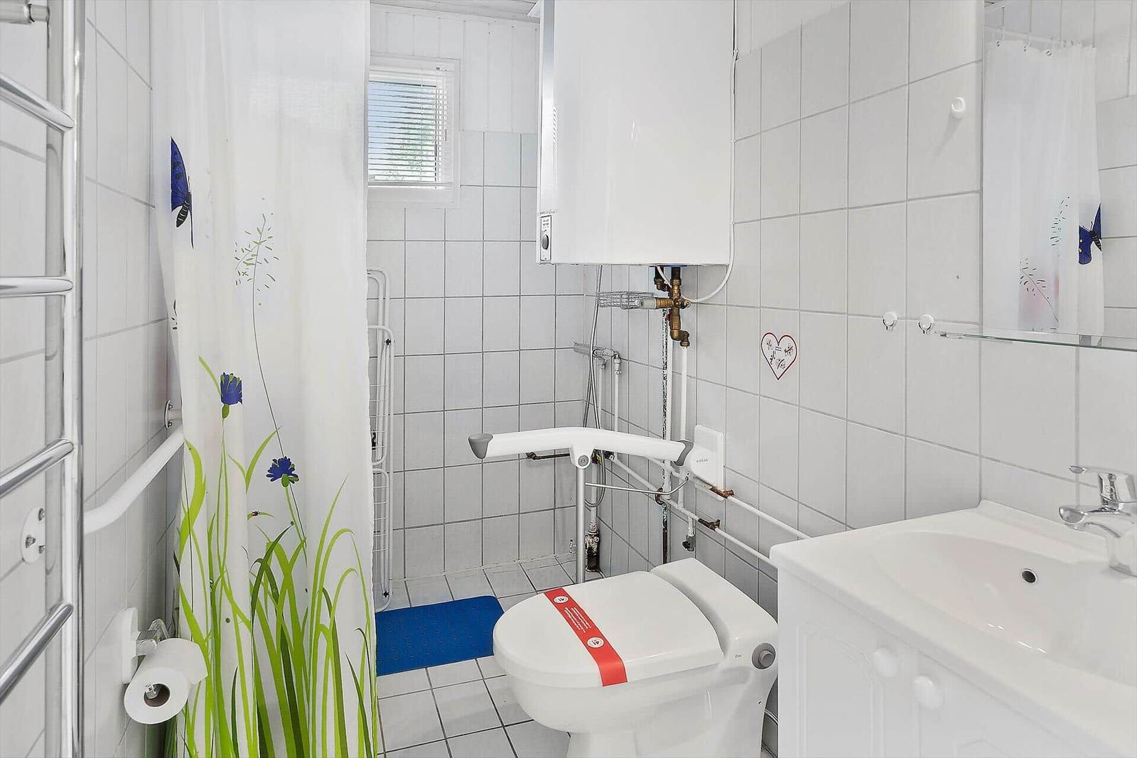 Badezimmer mit Toilette, Dusche und Waschbecken. Weiße Fliesen und Vorhänge mit Blumenmotiv.