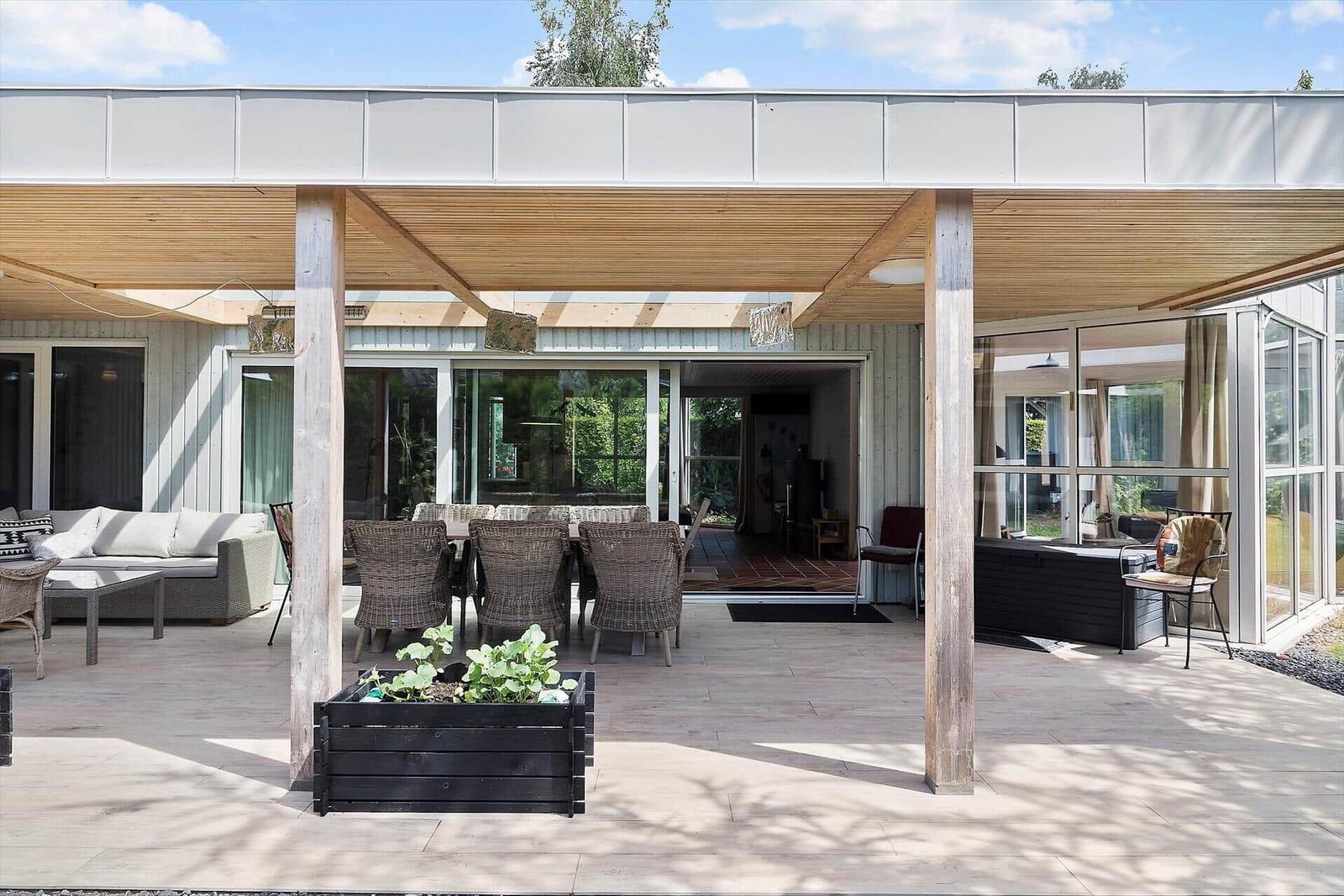 Terrasse mit Sitzgelegenheiten unter Holzüberdachung und Blick ins Haus.