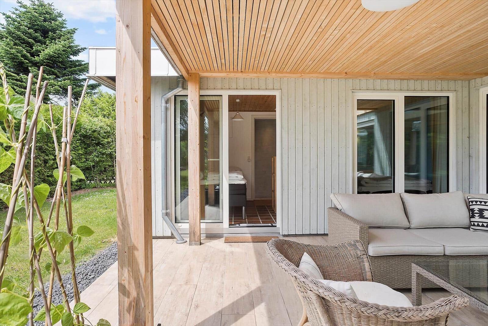 Terrasse mit Sitzgruppe, Glas-Türen zu Wohnbereich, Holzdecke und Gartenblick.