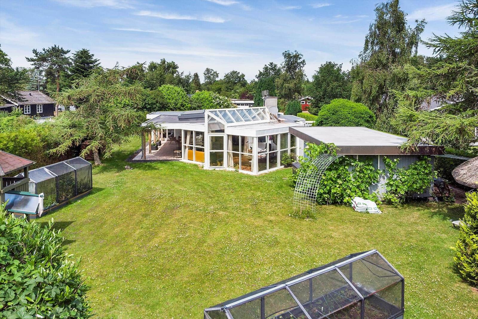 Modernes Haus mit großem Garten und Glasveranda. Umgeben von Bäumen und Grünflächen.