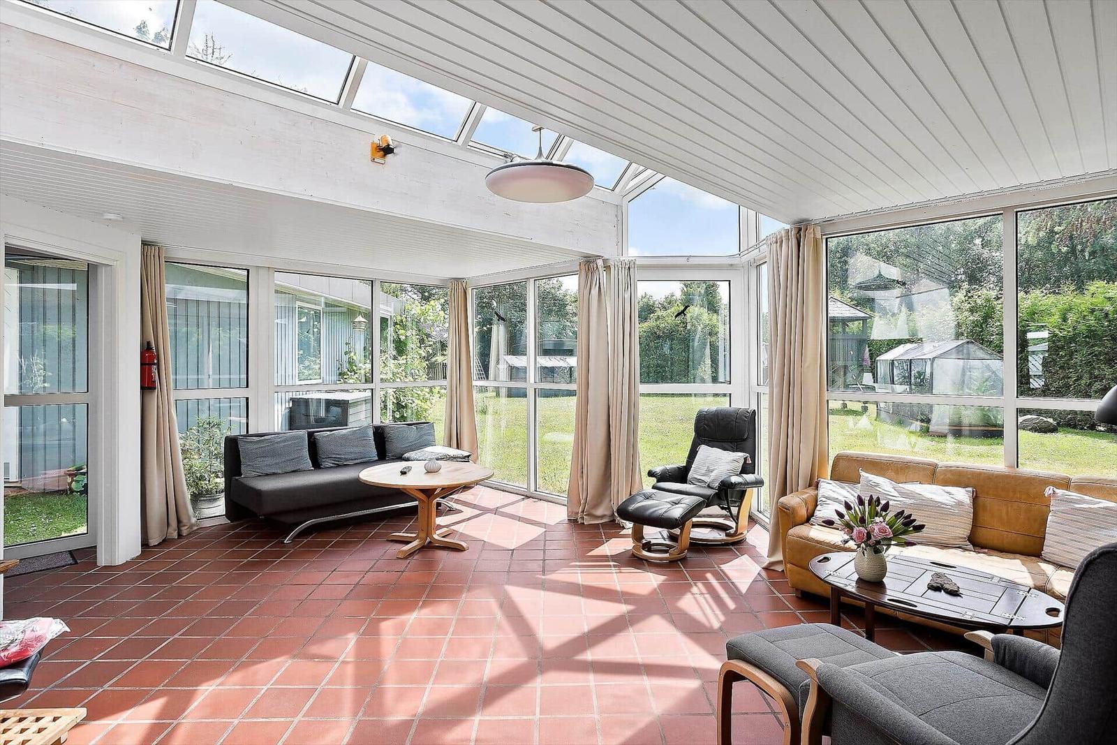 Großer Wohnbereich mit Glasfront, Sitzgruppe und Terrakottaboden. Blick auf Garten.