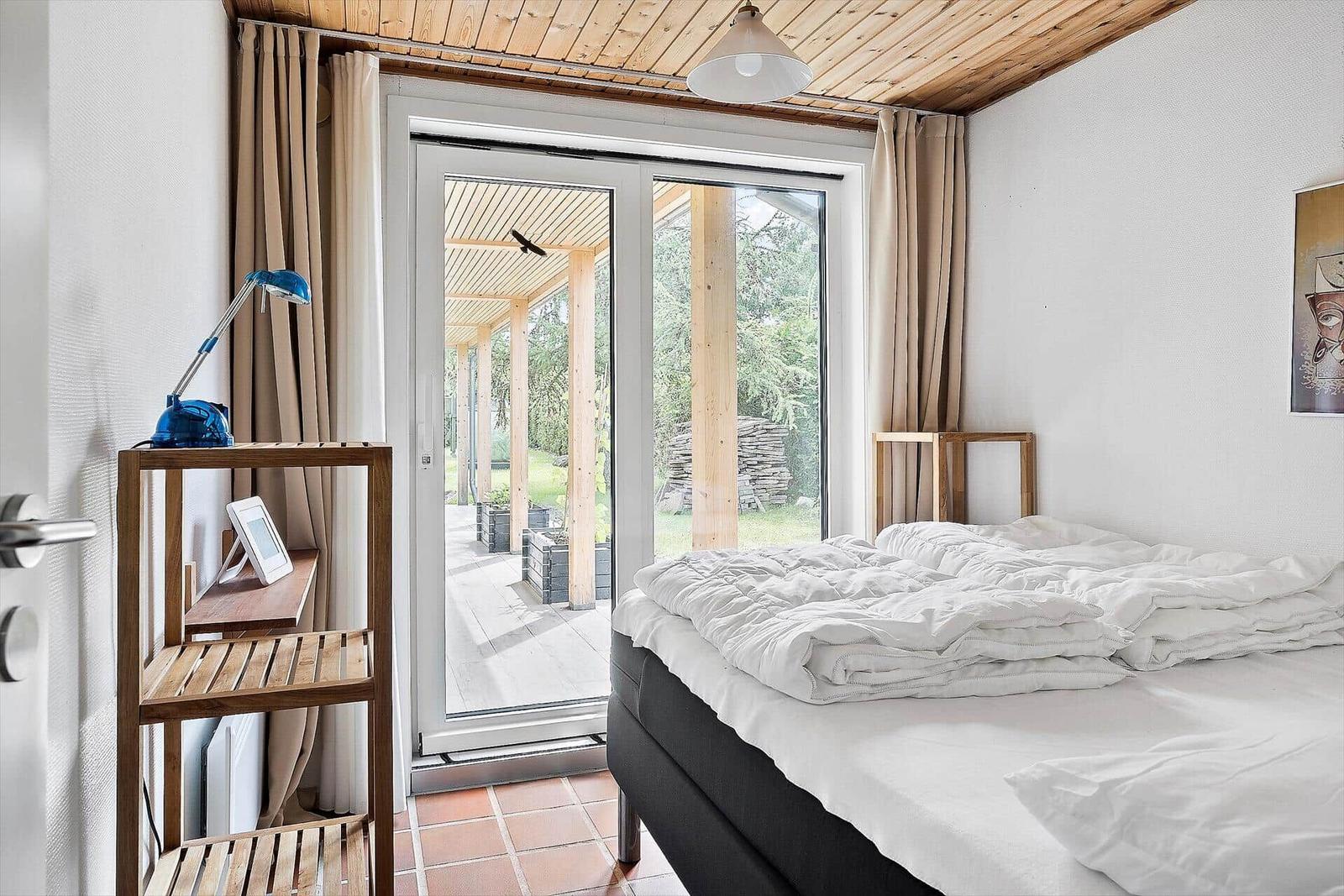 Schlafzimmer mit Bett, Holzregal und Glastür zum Außenbereich.