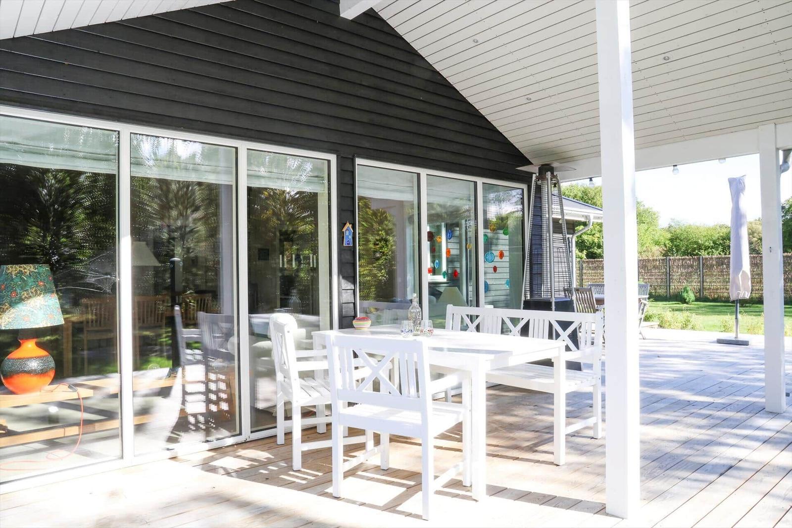 Terrasse mit weißem Tisch und Stühlen, Glasfront und Holzdielen.