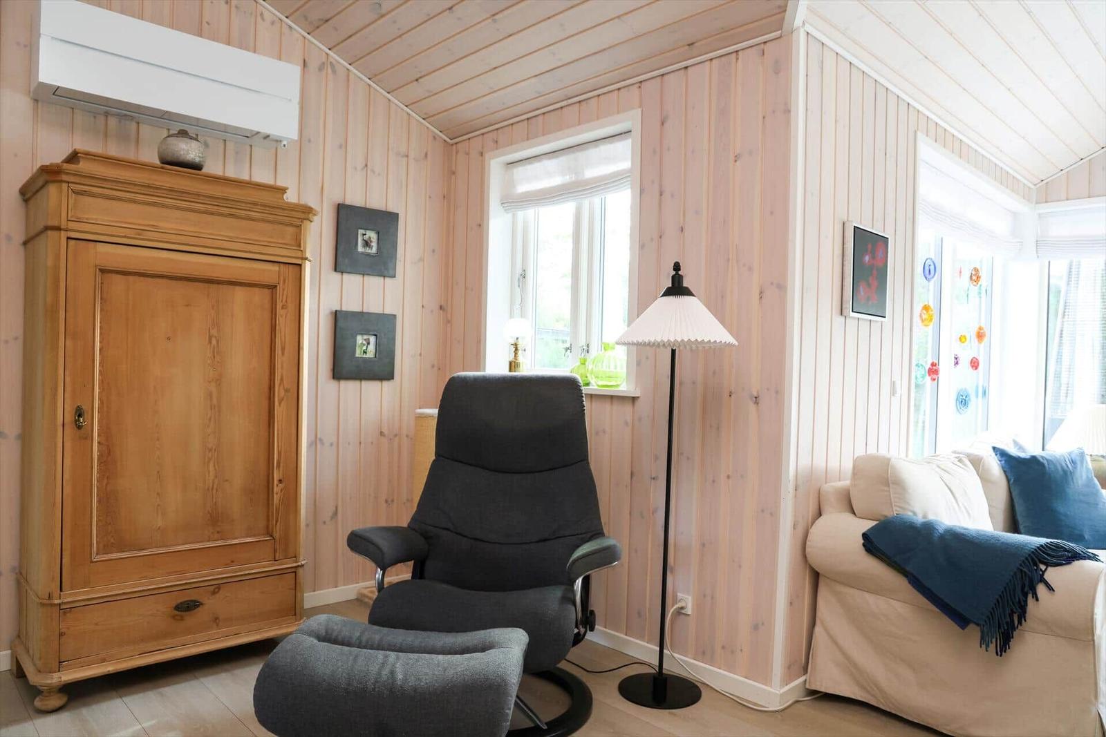 Ein Raum mit Holzwänden, einem grauen Sessel, einem Sofa und einem Holzschrank.